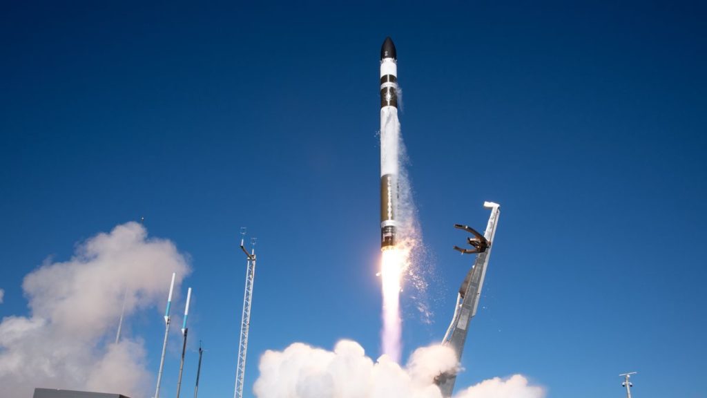 a white and black rocket launches into a blue sky.