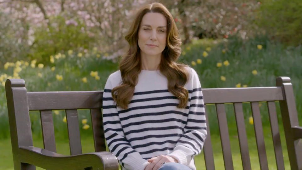 Kate Middleton, con indosso una camicia bianca a righe blu scuro, si siede su una panchina per annunciare che le è stato diagnosticato un cancro